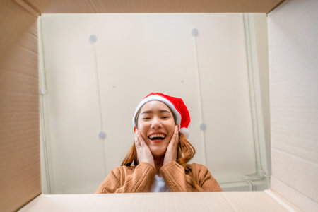 Low angle view of surprised young Asian woman wearing Christmas hat and unpacking. Opening carton...