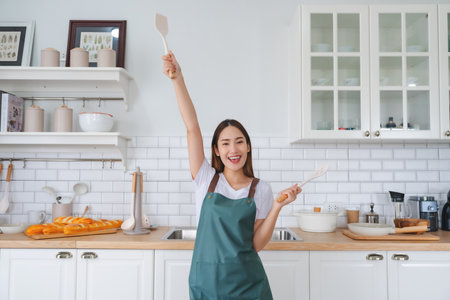 Young Asian woman dancing in the kitchen. The joy of a beautiful woman relaxing in her free time during the weekend in the houseの写真素材