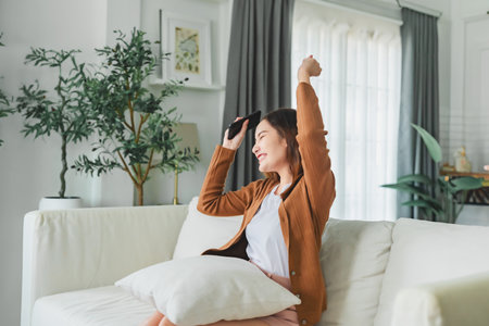 Happy young asian woman relax on comfortable couch at home texting messaging on smartphone, smiling girl use cellphone, chatting online message, shopping online from homeの写真素材