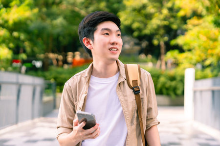 Portrait of handsome Asian student using smartphone. Young man walking outdoor happy smiling with holding mobile phoneの写真素材