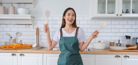 Young Asian woman dancing in the kitchen. The joy of a beautiful woman relaxing in her free time during the weekend in the houseの写真素材