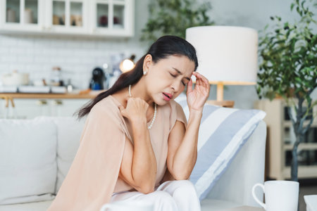 Upset Asian senior woman sitting on sofa, lost in thoughts, feeling lonely, disappointed, alone at home, unhappy, anxious, missing or sad. Senior woman experiencing mental health problemsの写真素材