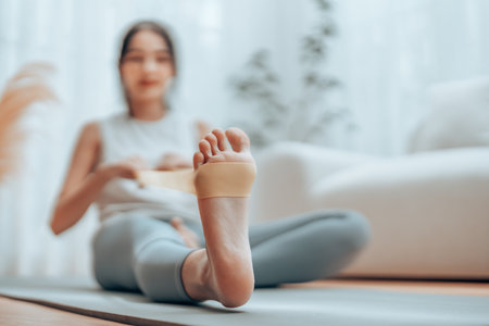Young Asian woman doing pilates workout using elastic strap pulling with arms for shoulder training on yoga mat indoors. Resistance band exercise at homeの写真素材