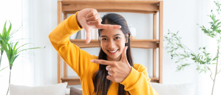 Young asian woman happy and making frame with fingers at living roomの写真素材