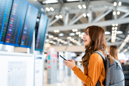 Young asian woman in international airport, using mobile smartphone and checking flight at the flight information boardの写真素材
