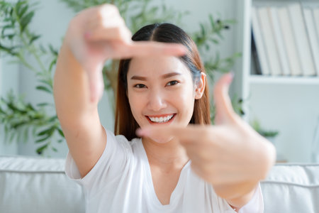 Young asian woman happy and making frame with fingers at living roomの写真素材