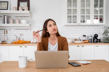 Asian young woman seriously working on computer laptop in house. She thinking find solution problem of workの写真素材