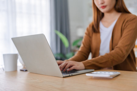 Young Asian woman working with laptop computer in home kitchen. Work at homeの写真素材