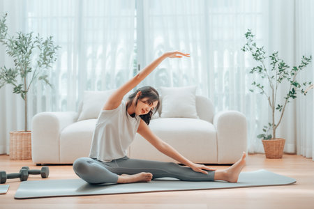 Happy young Asian woman practicing yoga and shoulder stretching at home sitting on floor in living roomの写真素材