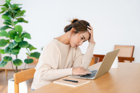 Thoughtful tired woman working on laptop computer looking on screen thinking solving problem at home office, serious woman search for inspiration make decision feel lack of ideasの写真素材