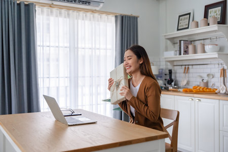 Young asian woman using computer laptop at home. Female showing gift box while on video conversation with friend. Happy birthday, Happy new year, Thanksgivingの写真素材
