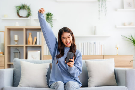 Happy young asian woman relax on comfortable couch at home texting messaging on smartphone, smiling girl use cellphone, chatting online message, shopping online from homeの写真素材