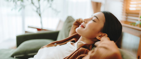 Relaxed young Asian woman enjoying rest on comfortable sofa, calm attractive girl relaxing on couch, breathing fresh air with eyes closed, meditating at homeの写真素材