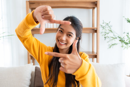 Young asian woman happy and making frame with fingers at living roomの写真素材