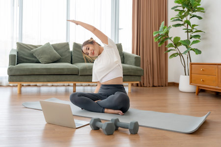 Happy young Asian woman practicing yoga and shoulder stretching at home sitting on floor in living roomの写真素材