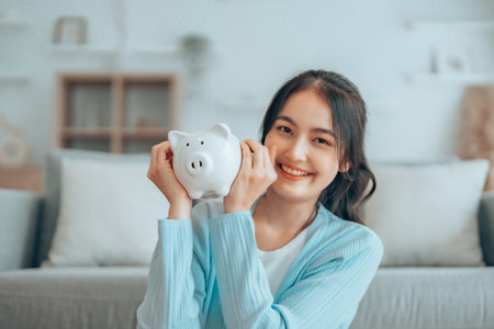 Young Asian woman holding piggy bank and sitting on the floor at home. Save money and financial investmentの写真素材