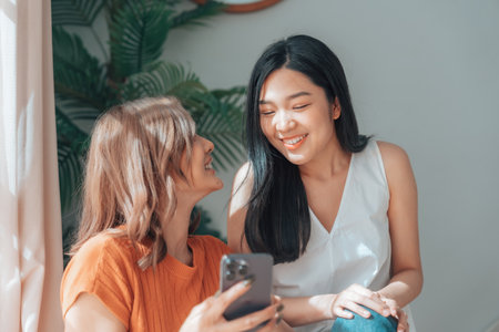 Two young Asian women smiling and happy while taking a selfie in their living room at home, video call, meeting conference, looking at the cameraの写真素材