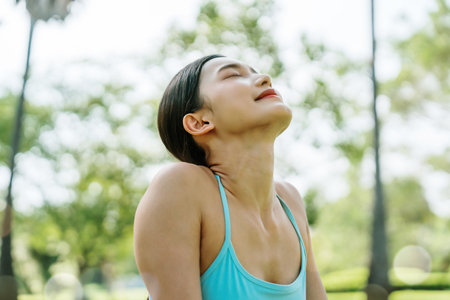 Young Asian woman relaxed breathing fresh air with trees in the background on a sunny day. Concept of wellness, healthy lifestyle, mindfulness, and outdoor fitnessの写真素材