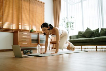 Young Asian woman doing sport exercises indoor. Beautiful girl workout at home. Athletic outfit is doing mountain climber exercisesの写真素材