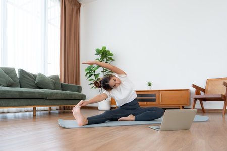 Young Asian woman stretching yoga workout on exercise mat while online training class with computer laptop in living roomの写真素材