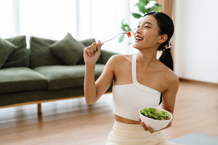 Healthy Asian Woman Enjoying Fresh Salad at Home After Yoga Workoutの写真素材