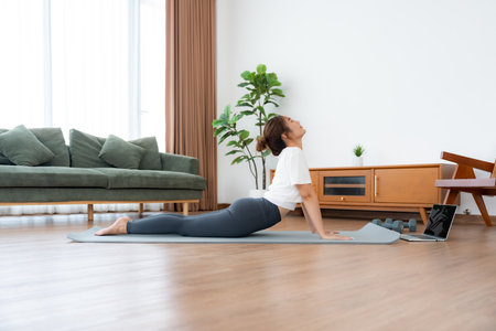 Young Asian woman stretching yoga workout on exercise mat while online training class with computer laptop in living roomの写真素材