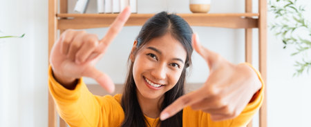 Young asian woman happy and making frame with fingers at living roomの写真素材