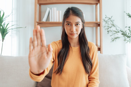Young Asian woman with serious expression raising her hand stop gesture. Concept of protest against harassment, discrimination, and violation of human rights. Symbol of resistance and social justiceの写真素材