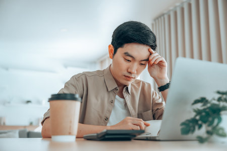 Asian man are stressed, pain in their eyes, working on laptop in living room at homeの写真素材