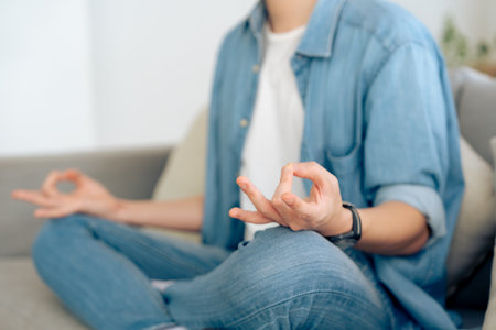 Young Asian man practicing yoga and meditation at home sitting on floor in living room in lotus position and relaxing with closed eyes. Mindful meditation and wellbeing conceptの写真素材