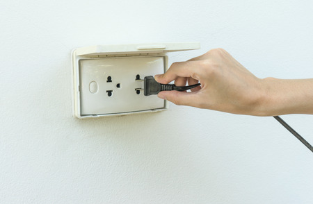 Female hand plugging in appliance to electrical outlet in wall
