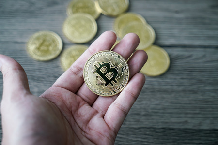 hand with golden bitcoin coin on the wooden table