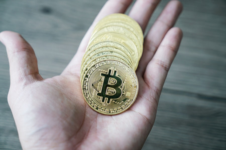 hand with golden bitcoin coin on the wooden tableの写真素材