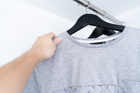 A hand taking a grey shirt, gray shirts hanging in a rowの写真素材
