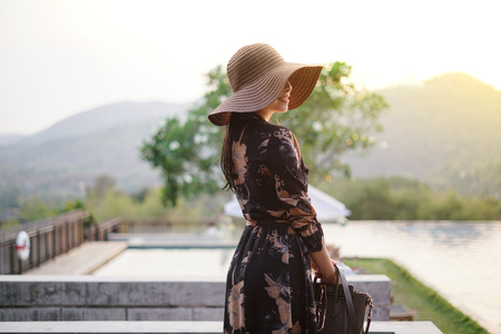Beautiful attractive woman at the swimming terrace with oversize hat over her eyes, wearing a long dressの写真素材