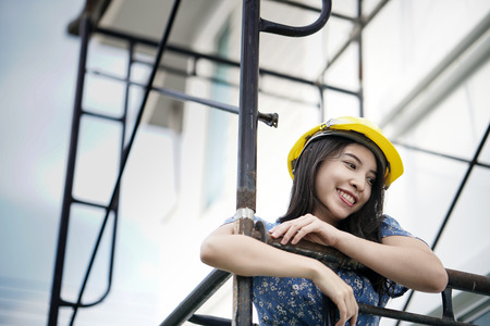 Asian woman engineer in blue dress, yellow helmet safety standing with scaffoldの写真素材
