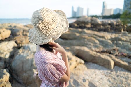 Back view of young woman sitting on the rock at the beachの写真素材