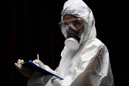Woman wearing gloves with biohazard chemical protective suit and mask. is writing report on paper.