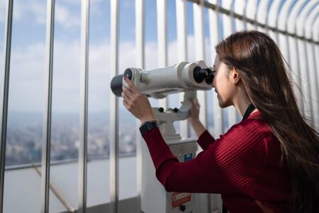 Close up of a woman looking to the city by telescope (the binoculars) on the top of building.の写真素材