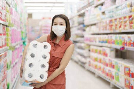 covid-19 spreading outbreak. Woman in medical protective mask panic buying tissue paper. Fear of coronavirus.の写真素材