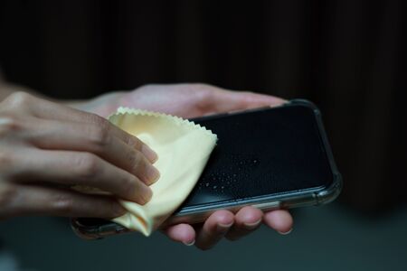 Hand holding and cleaning mobile phone screen with a napkin  for corona virus or Covid-19...