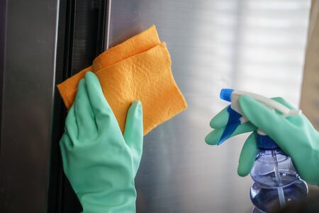 Women hands in rubber green gloves cleaning the Refrigerator at home kitchen,  for corona virus or Covid-19 protection.の写真素材