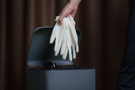 Hand putting used dirty surgical glove to  a garbage bin. Mask protect dust and corona virus in...