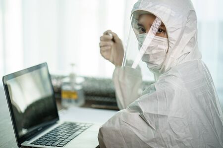 Woman in protective hazmat suit worker  in laboratory computer analyzing in laboratory. to stop spreading  coronavirus or COVID-19.の写真素材