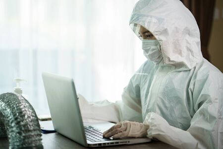 Woman in protective hazmat suit worker  in laboratory computer analyzing in laboratory. to stop spreading  coronavirus or COVID-19.の写真素材
