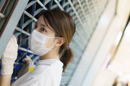 Woman wearing  protective mask and gloves looking at closed shop, coronavirus pandemic.の写真素材