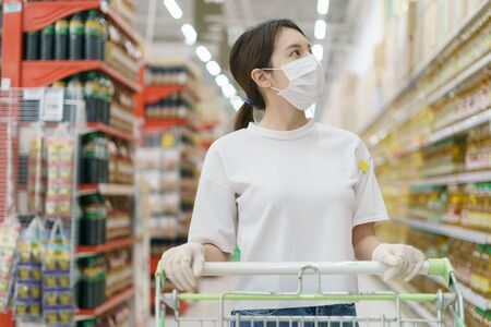 Woman wearing surgical mask and gloves with a shopping trolley, shopping during a Coronavirus  pandemic.の写真素材