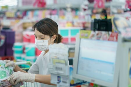 Woman protects herself from corona infection with surgical mask and gloves at cashier scanning...