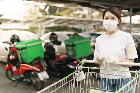 Woman with a shopping trolley outside the store, wearing surgical mask during a coronavirus...