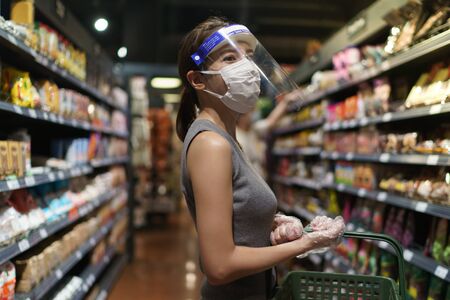 Woman wearing gloves, face shield and mask. Panic shopping during the corona virus pandemic.